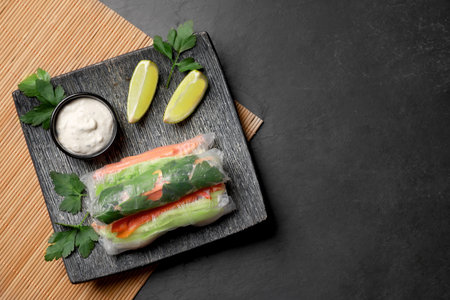 Delicious rolls wrapped in rice paper served on black table, top view. Space for text
