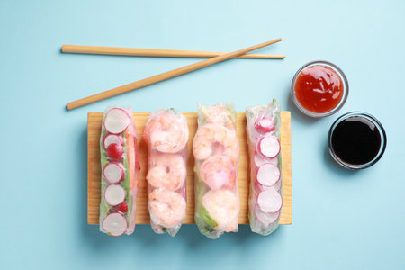 Different delicious spring rolls, chopsticks and sauces on light blue background, flat layの写真素材