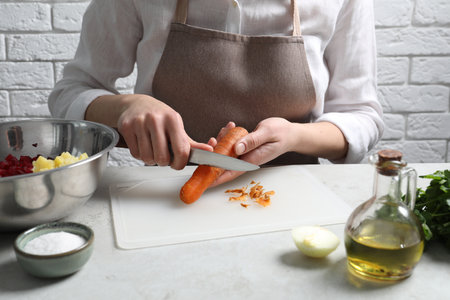 Woman peeling boiled carrot at white table, closeup. Cooking vinaigrette saladの写真素材