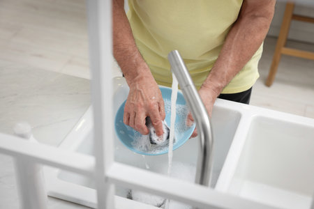 Closeup of man washing plate above sink in kitchen, view from outsideの写真素材