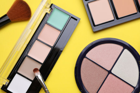 Different contouring palettes and brushes on yellow background, flat lay. Professional cosmetic productの写真素材