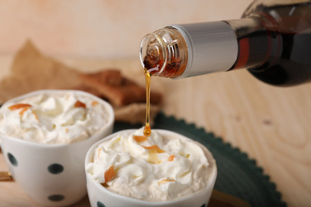 Pouring delicious caramel syrup into cup with coffee and whipped cream at wooden table, closeupの写真素材