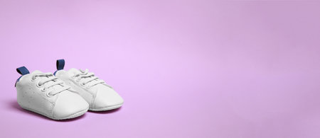 Cute baby shoes on violet background, space for text. Banner design