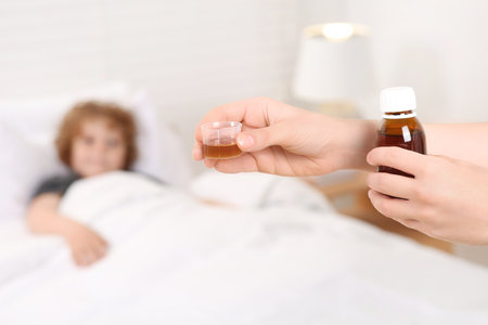 Mother with cough syrup for her son in bedroom, focus on handsの写真素材