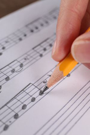 Woman writing musical notes with pencil on sheet of paper, closeupの写真素材