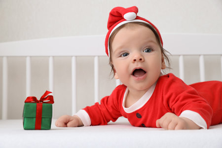 Cute baby wearing festive Christmas costume with gift box in crib