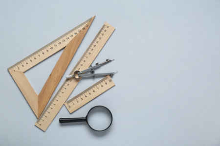 Different rulers, magnifying glass and compass on light gray background, flat lay. Space for text