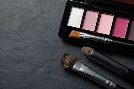 Beautiful eye shadow palette and brushes on dark gray textured table, flat lay. Space for textの写真素材