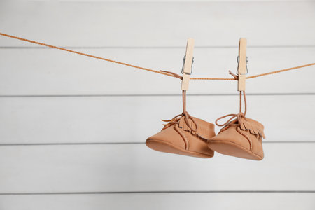 Cute baby shoes drying on washing line against white wall. Space for textの写真素材