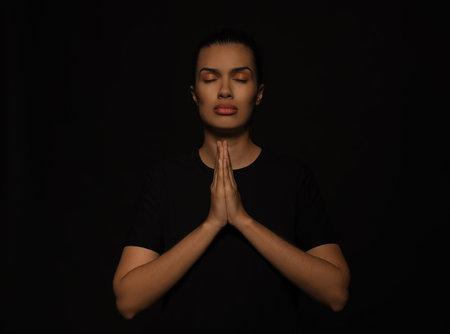 African American woman with clasped hands praying to God on black backgroundの写真素材