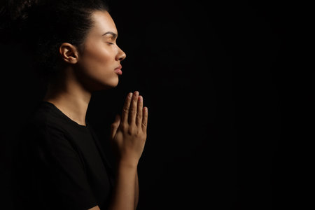 African American woman with clasped hands praying to God on black background. Space for textの写真素材