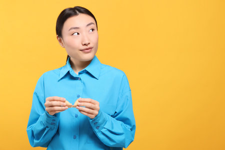 Asian woman breaking tasty fortune cookie with prediction on yellow background, space for textの写真素材