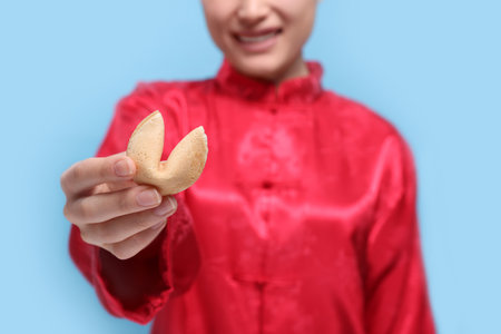 Young woman holding tasty fortune cookie with prediction on light blue background, closeupの写真素材