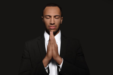 African American man with clasped hands praying to God on black backgroundの写真素材