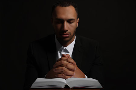 African American man with Bible praying to God on black backgroundの写真素材