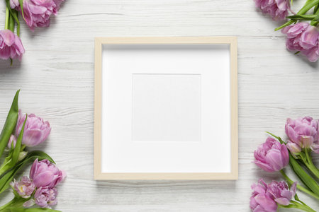 Empty photo frame and beautiful flowers on white wooden table, flat lay. Space for design