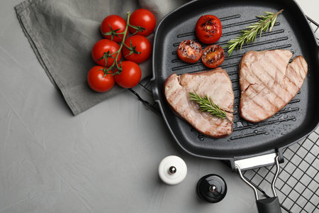 Delicious tuna steaks with rosemary and tomatoes on gray table, flat lay. Space for textの写真素材