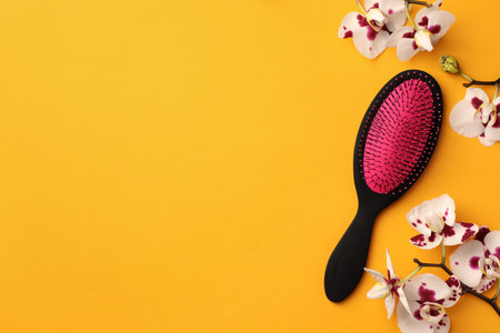 Stylish hairbrush and orchid flowers on yellow background, top view. Space for textの写真素材