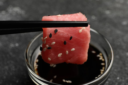 Dipping tasty sashimi (piece of fresh raw tuna) into soy sauce at black table, closeupの写真素材