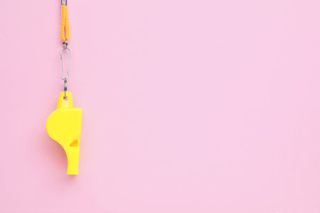 One yellow whistle with orange cord on pink background, top view. Space for textの写真素材