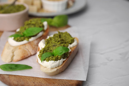 Tasty bruschettas with cream cheese, pesto sauce and fresh basil on white table, closeup. Space for textの写真素材