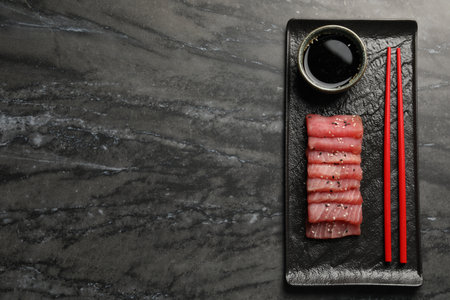 Tasty sashimi (pieces of fresh raw tuna with sesame seeds) and soy sauce on black marble table, top...