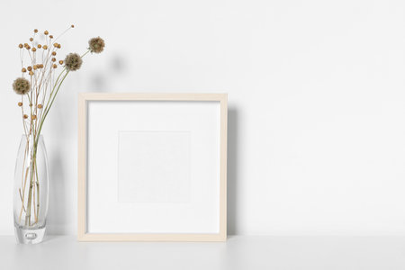 Empty photo frame and vase with dry decorative flowers on white table. Mockup for designの写真素材