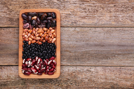 Plate with different kinds of dry kidney beans on wooden table, top view. Space for textの写真素材