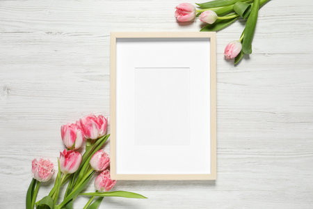 Empty photo frame and beautiful flowers on white wooden table, flat lay. Space for design