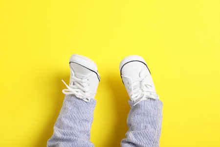 Little baby in stylish gumshoes on yellow background, top view. Space for textの写真素材