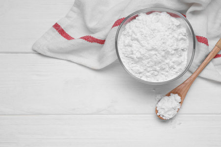 Bowl and spoon of starch on white wooden table, top view. Space for text