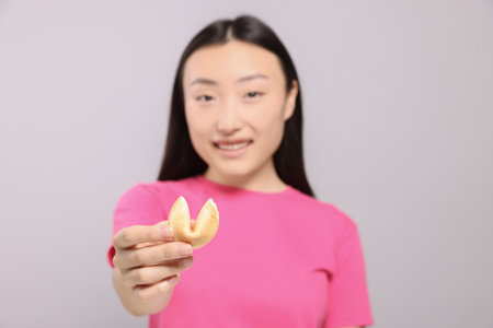 Asian woman against grey background, focus on tasty fortune cookie with predictionの写真素材