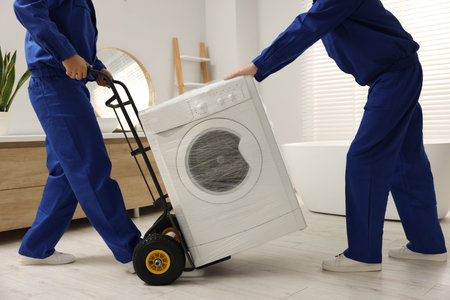 Male movers carrying washing machine in bathroom, closeup. New houseの写真素材