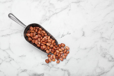 Metal scoop with dry kidney beans on white marble table, flat lay. Space for text