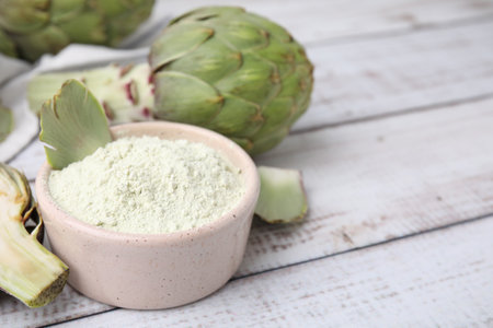 Bowl with powder and fresh artichokes on white wooden table, closeup. Space for textの写真素材