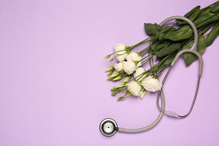 Stethoscope and beautiful flowers on light violet background, flat lay with space for text. Happy Doctor's Dayの写真素材