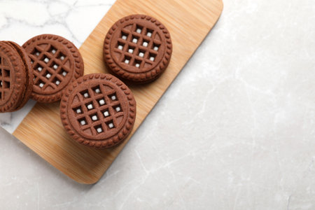 Tasty chocolate sandwich cookies with cream on light gray marble table, flat lay. Space for text