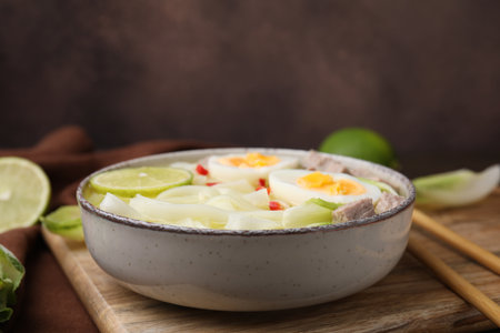Bowl of delicious rice noodle soup with meat and egg on wooden board, closeup