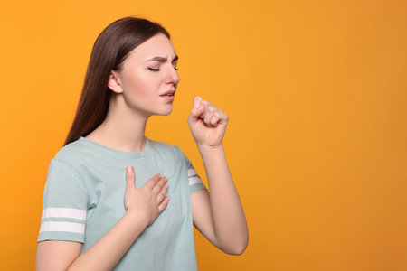 Young woman coughing on orange background, space for text. Sore throatの写真素材
