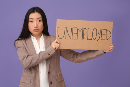 Asian woman holding sign with word Unemployed on purple backgroundの写真素材