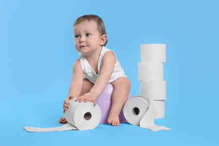 Little child sitting on baby potty and stack of toilet paper rolls against light blue backgroundの写真素材