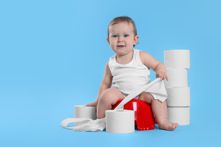 Little child sitting on baby potty and stack of toilet paper rolls against light blue background. Space for textの写真素材