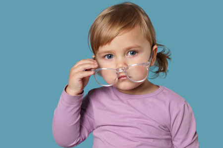 Cute little girl with glasses on light blue backgroundの写真素材