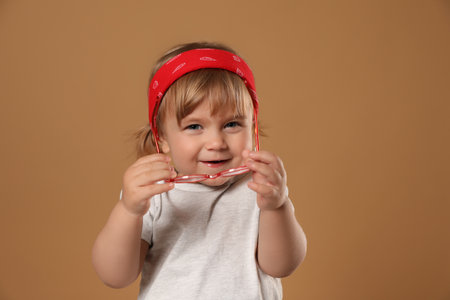 Cute little girl in glasses on pale brown background