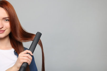 Beautiful woman using hair iron on light gray background, closeup. Space for textの写真素材