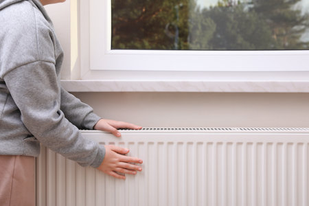 Girl warming hands on heating radiator indoors, closeupの写真素材