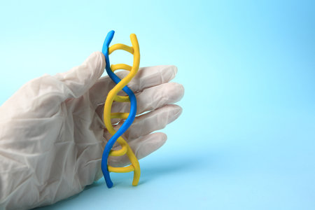 Scientist with DNA molecule model made of plasticine on light blue background, closeup. Space for textの写真素材