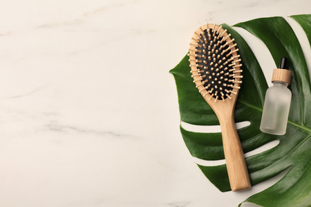 Wooden hair brush, bottle of essential oil and monstera leaf on white marble table, top view. Space for textの写真素材