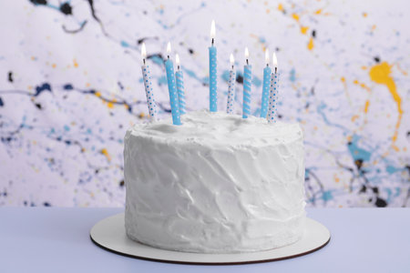 Delicious cake with cream and burning candles on light blue tableの写真素材