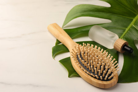 Wooden hair brush, bottle of essential oil and monstera leaf on white tableの写真素材